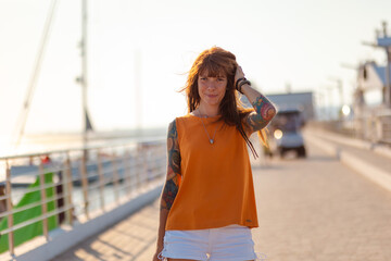 Obraz premium Portrait of young Caucasian woman with tattoo smiling and posing on pier. Concept of freedom and happiness