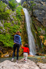 Naklejka na ściany i meble Mother with her son Grunas waterfall of Theth national park in summer, Albania. Albanian alps