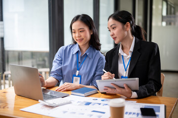 A beautiful young Asian businesswoman is looking at a laptop screen, discussing work.