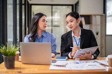 Two focused Asian businesswomen or female accountants are discussing work, examining financial data