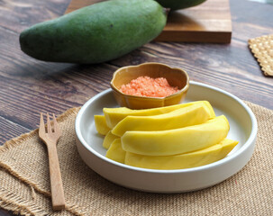 Pickled mango served with chili sugar dip in white plate of wood table - Preservative food concept 