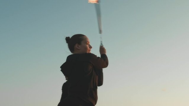 Medium shot of two Caucasian professional circus artists juggling and dancing with fire while showing fore show at summer festival outdoors at sunset