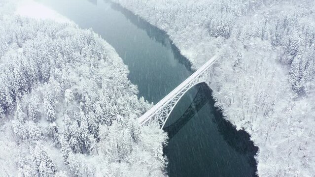 Drone Aerial view Landscape of Railway bridge between the mountain over the river in snow day. Pine tree forest mountain with railroad track covered in snow. Beautiful scenic nature in winter season.