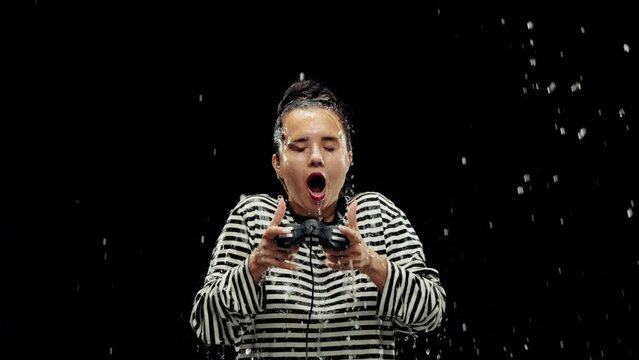 Young woman emotionally playing online video games on console on backg background. Water splashing into face. Concept of emotions, relaxation, stress, leisure activity, ad