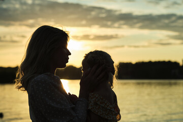 silhouettes of a mother and child embracing at a lake during sunset evoke a sense of peace that...
