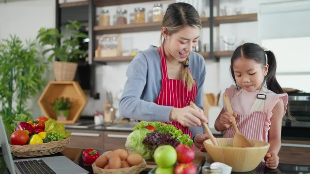 Happy Asian mother and daughter enjoy making tasty salad in kitchen room at home. Beautiful young mother and daughter cooking together. Healthy food concept, Family Activity concept 