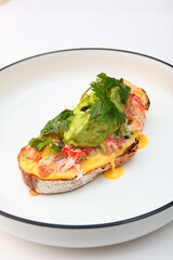 Crab meat bruschetta. Served on white plate with mashed avocado, tomatoes and herbs. Mediterranean street food: crab meat sandwich.Isolated object.Vertical photo.