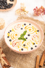 Yoghurt with bilberry and caramel in ceramic bowl on gray concrete, side view, selective focus.