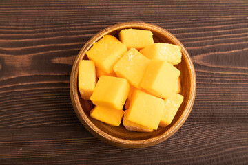 Dried mango cubes in wooden bowls on brown wooden, top view