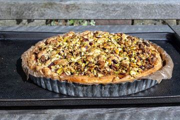 Home baked plum pie with pistachio crumble topping on a baking tray outdoors
