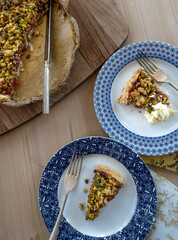Slices of plum pie with a pistachio crumble topping served on attractive plates with clotted cream...