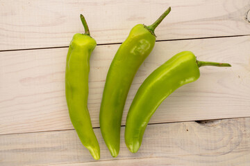 Three green chili peppers on a wooden table, macro, top view.