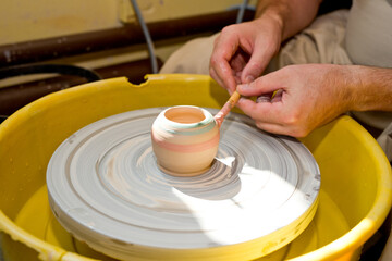 The hands of a potter sculpting a piece of clay on a rotating potter's wheel.