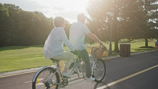 Casually dressed couple cycling on tandem bike outdoors