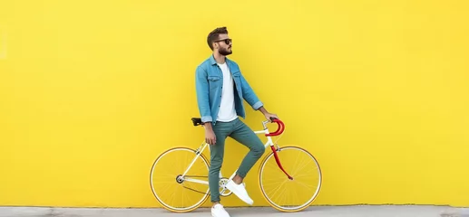 Papier Peint photo Lavable Vélo Side view of a young hipster man with a fixed bike near the yellow wall