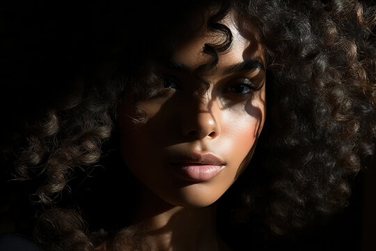 Beauty portrait afro american sensual woman model with curly hair looking at camera, closeup shadow on female face, femininity