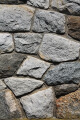 Closeup of solid rock wall with irregular shaped stones and contrasting dark gray mortar