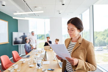 Businesswoman reading document while colleagues discussing in conference room at office