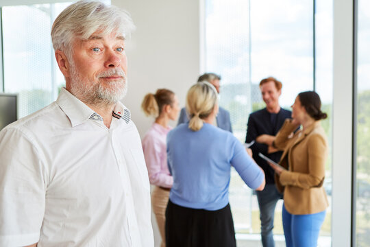Thoughtful senior businessman with white hair and beard standing against team discussing at workplace