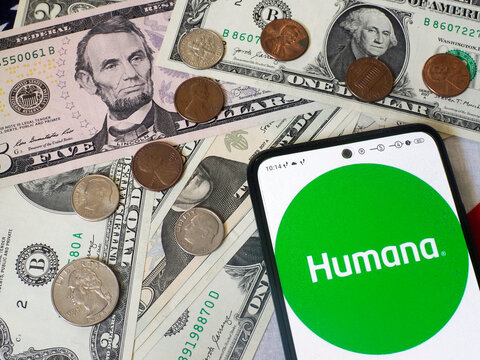 In this photo illustration,  Humana Inc. logo is seen displayed on a smartphone and US currency notes and coins in the background.