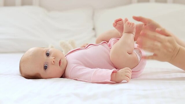 a small newborn baby girl lies on a white cotton bed at home, mother's hands stroke or do foot massage
