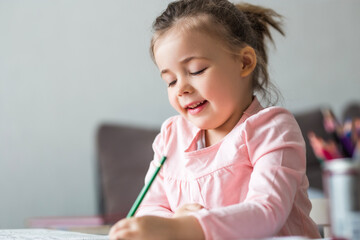 Cute smiling little girl write homework  at desk at home. Happy preschooler writing with left hand...