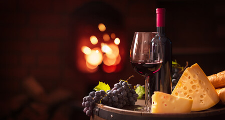 A glass of red wine with grapes and cheese on the background of a home fireplace. Wine tasting