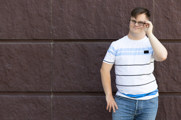 Smiling young man with down syndrome in glasses posing against stone wall background, place for text