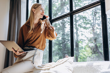 Young woman talking on the phone and checking information on laptop