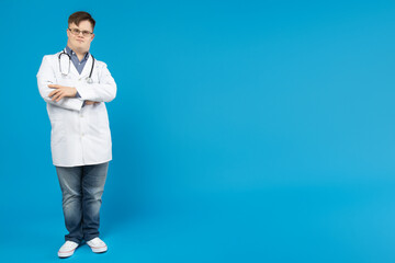 Smiling young man with down syndrome wearing glasses in doctor uniform with stethoscope, place for...