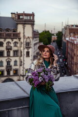 Fototapeta premium Beautiful girl with lilacs on the roof at sunset in summer