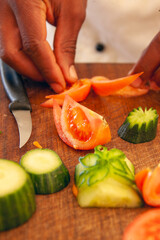 african american chef cutting  and garnishing cucumbers and tomatoes for a vegetarian meal on a wooden chopping board