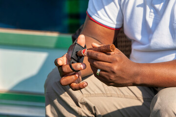 african american businessman sited outdoors using a Guillotine cigar cutter to cut a premium cigar