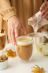Pumpkin coffee, leaves, gift box and female hands on white background