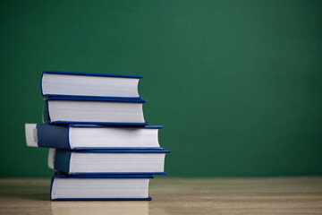 Stack of books on wooden table over classroom blackboard. Education background. Back to school concept.