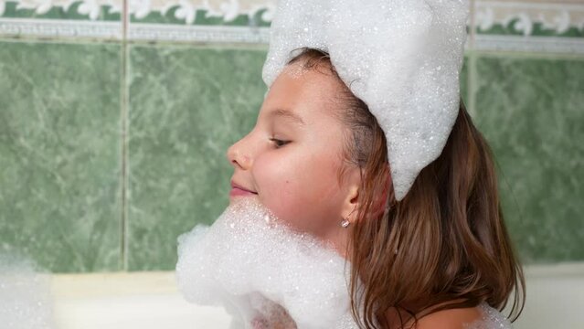 Cute girl playing with soap foam in the bath