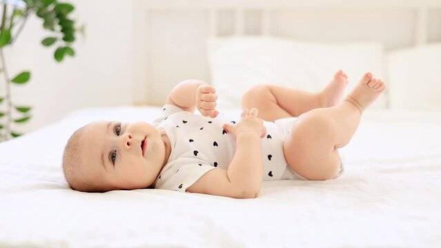 laughing little baby girl of six months on a bed in a bright bedroom on the back, close-up of a smiling baby on a white background