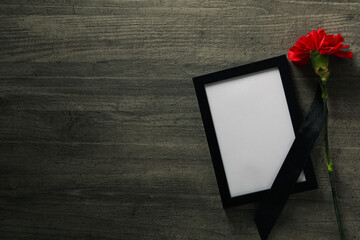 Photo frame with black ribbon and flower on wooden background, space for text