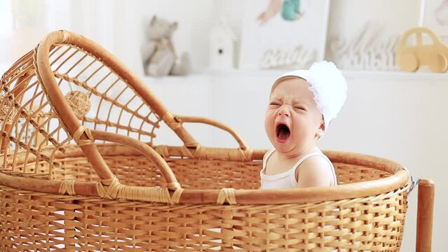 a crying little baby in a cradle or crib in the nursery, a baby girl in a white bodysuit screams and cries, calling for her mother