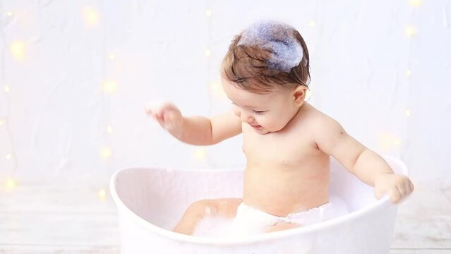 a joyful baby girl of six months is bathing in a bubble bath, a small child is having fun playing with water, the concept of care and hygiene