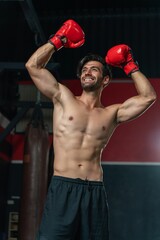 Handsome man with a muscular body showing winner pose cheering happily, displaying his boxing prowess in a boxing gym studio