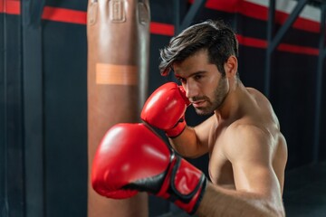 Handsome Middle Eastern man with a muscular body physique showing how to throws powerful punches at a punching bag, displaying his boxing prowess in a boxing gym