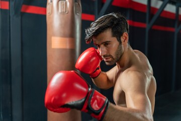 Handsome Middle Eastern man with a muscular body physique showing how to throws powerful punches at a punching bag, displaying his boxing prowess in a boxing gym