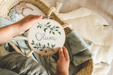 Pregnant woman holding a handmade embroidery with the name Olivia in her hands, concept in...