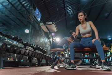 Fototapeta na wymiar Determined young Asian woman strengthens her arm with single-arm dumbbell rows on the bench press, showing her dedication to building muscle at the gym