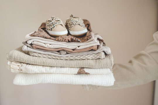 Stack of baby clothes in hand on neutral background