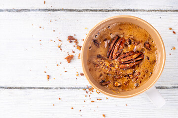 Autumn winter hot spicy drink, Maple Pecan coffee cup on white wooden table with cozy sweater and ingredients copy space