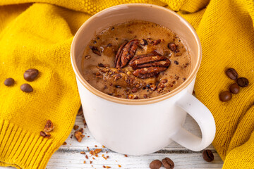 Autumn winter hot spicy drink, Maple Pecan coffee cup on white wooden table with cozy sweater and ingredients copy space