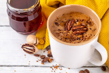 Autumn winter hot spicy drink, Maple Pecan coffee cup on white wooden table with cozy sweater and ingredients copy space