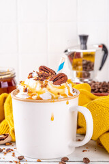 Autumn winter hot spicy drink, Maple Pecan coffee latte with whipped cream cup on white wooden table with cozy sweater and ingredients copy space